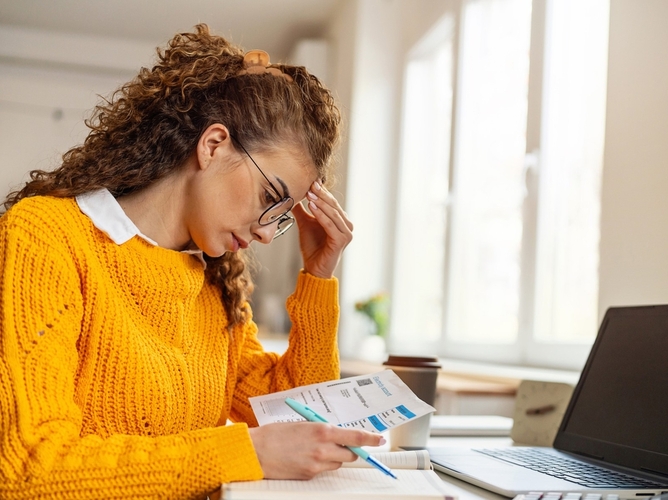 woman in orange sweater stressed reviewing financial documents